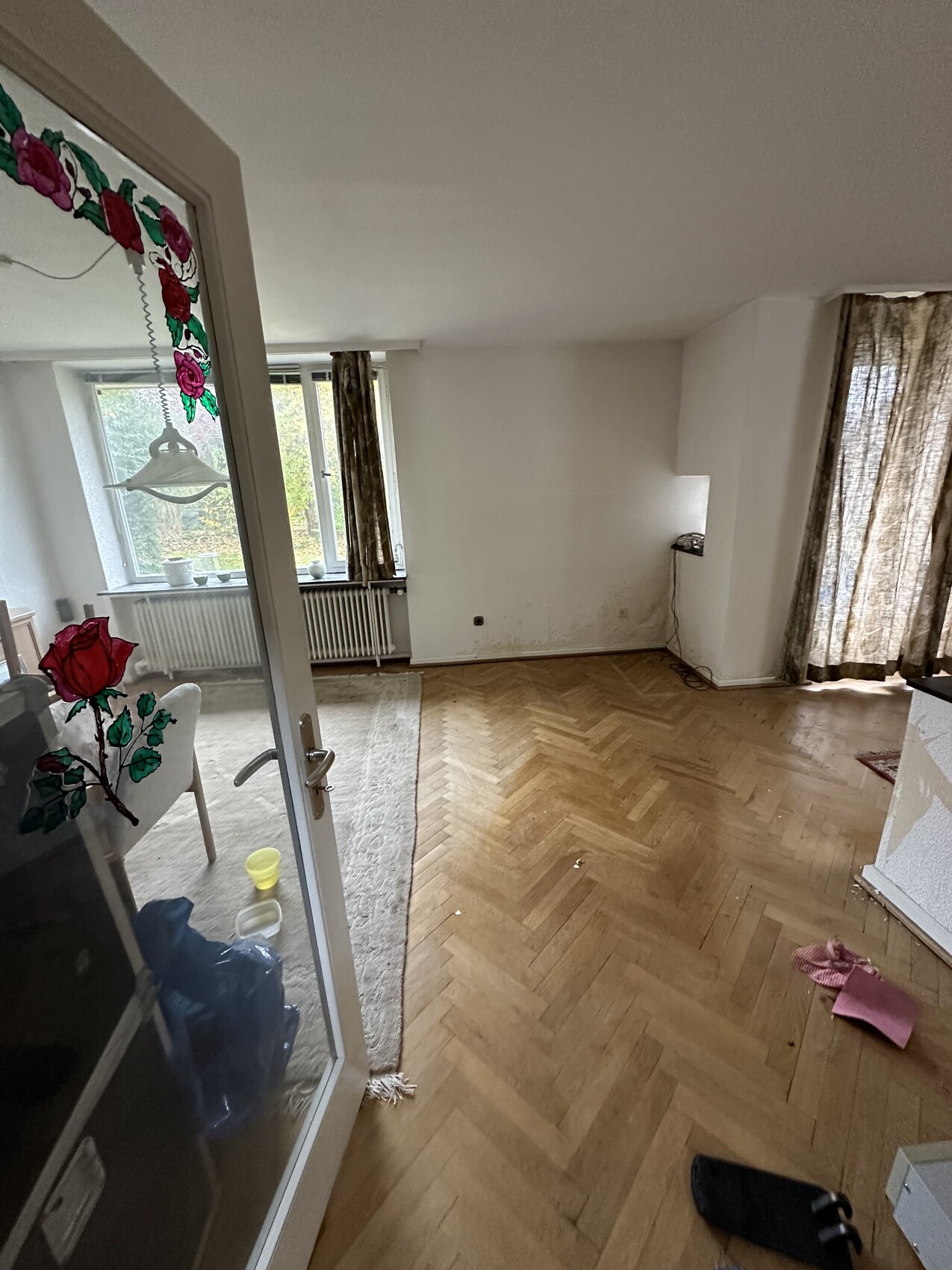 Helles Wohnzimmer mit Holzboden, Fensterfront/Vorhängen; Glastür mit Rosen-Aufkleber.