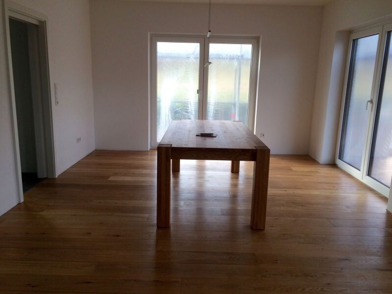 Helles Wohnzimmer mit Holztisch, Holzboden und grossen Terrassentueren