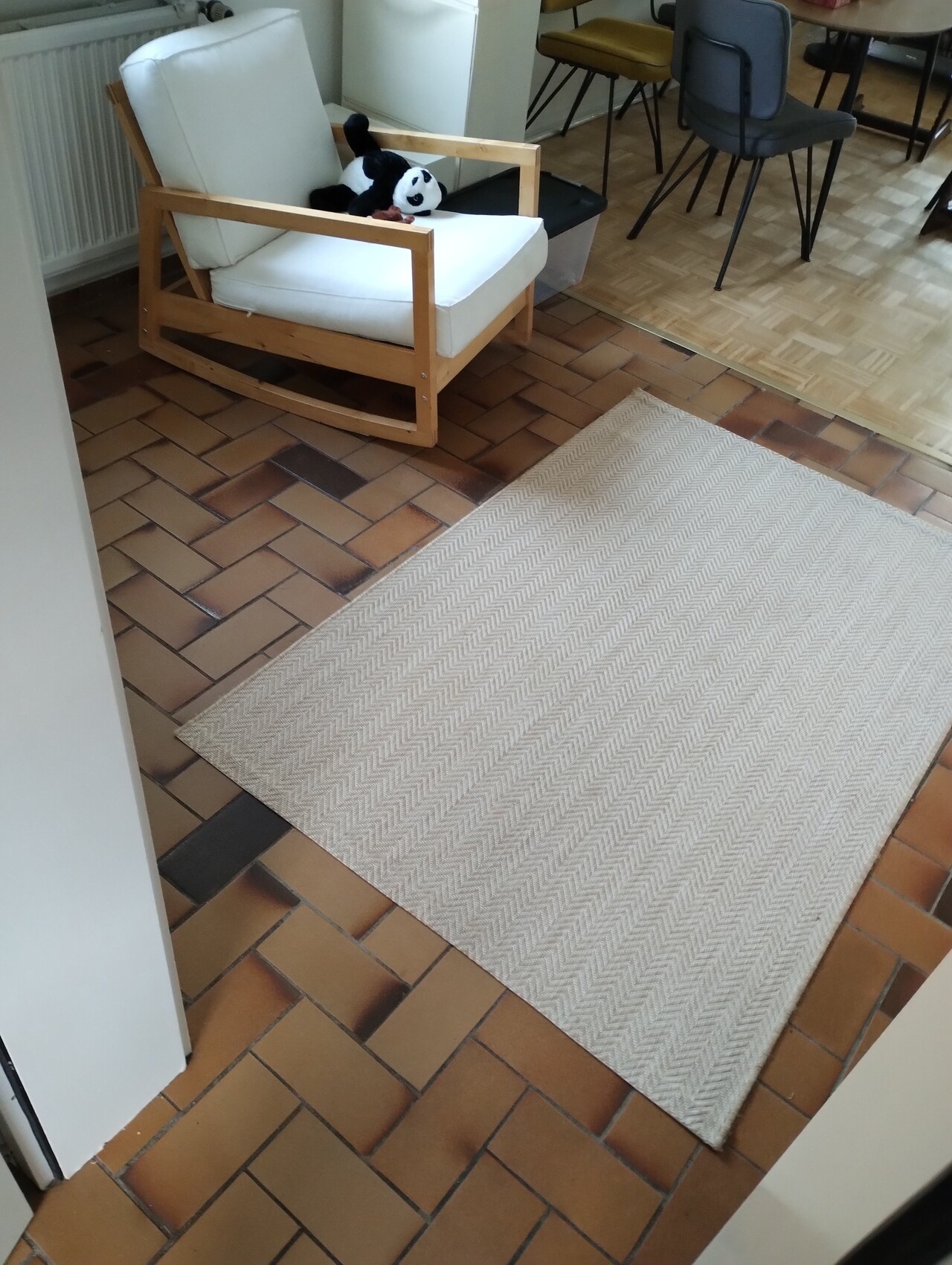 Holzrahmen-Sessel mit weißem Bezug, Panda-Plüschtier darauf; braune Fliesen und beige Teppich im Raum.