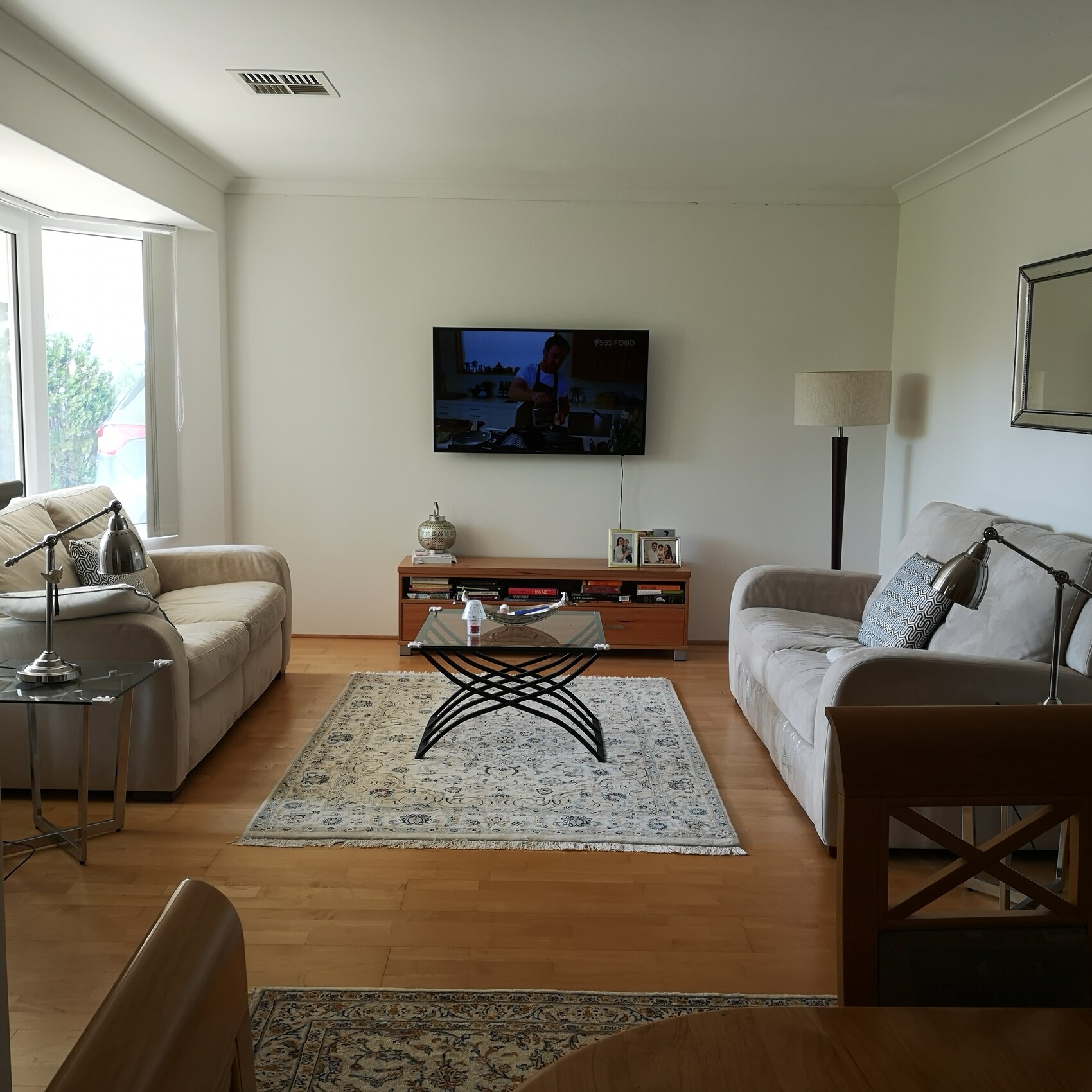 Wohnzimmer mit zwei hellen Sofas, Glas-Couchtisch, Fernseher an der Wand und Teppich