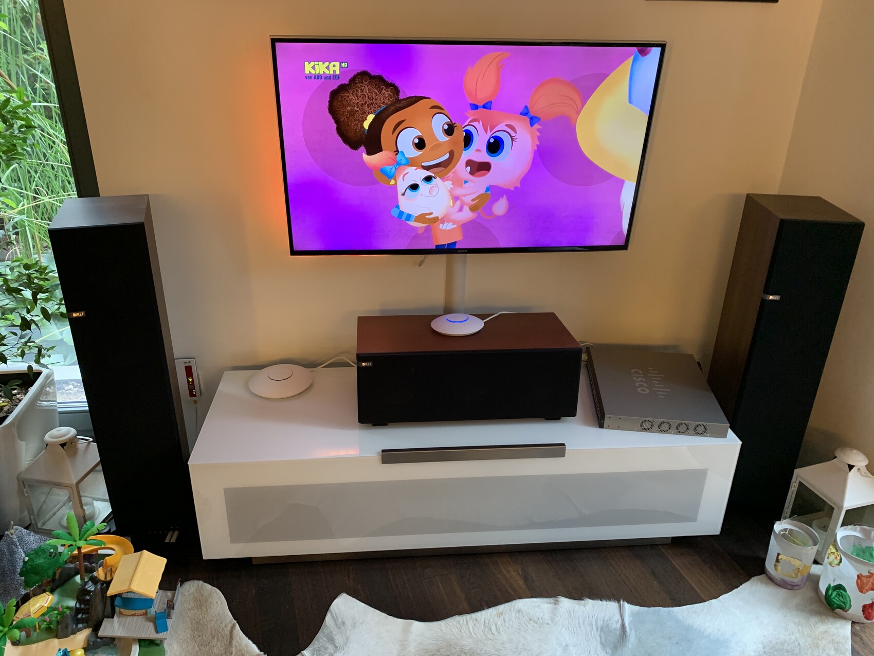 Fernseher mit buntem Kinder-Animation-Bild, zwei Standlautsprecher flankieren weiße Kompaktanlage.