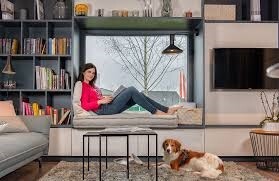 Frau sitzt auf Fensterbank im Wohnzimmer, neben einem Hund auf dem Boden.