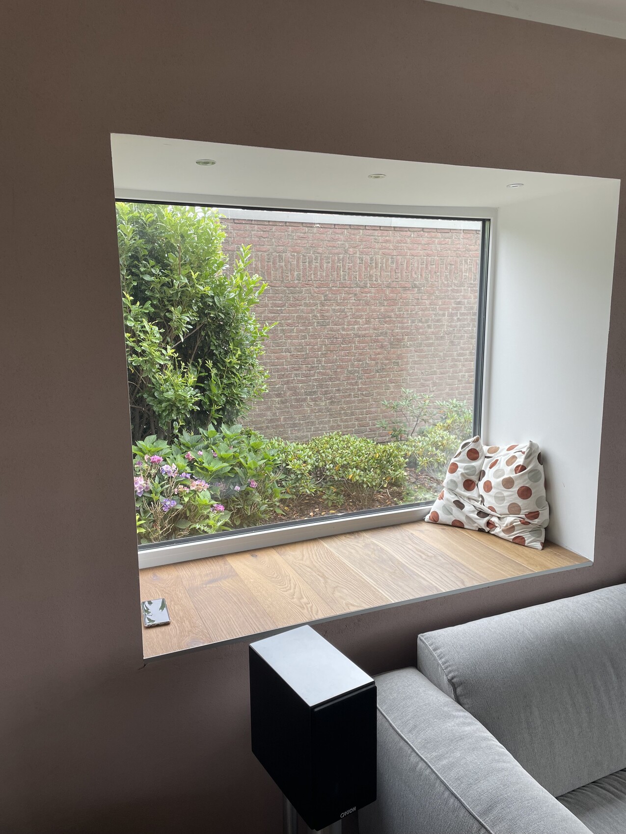 Innenfenster-Nische mit Holzbank und Kissen mit Punkten; Blick auf Garten und Backsteinmauer.