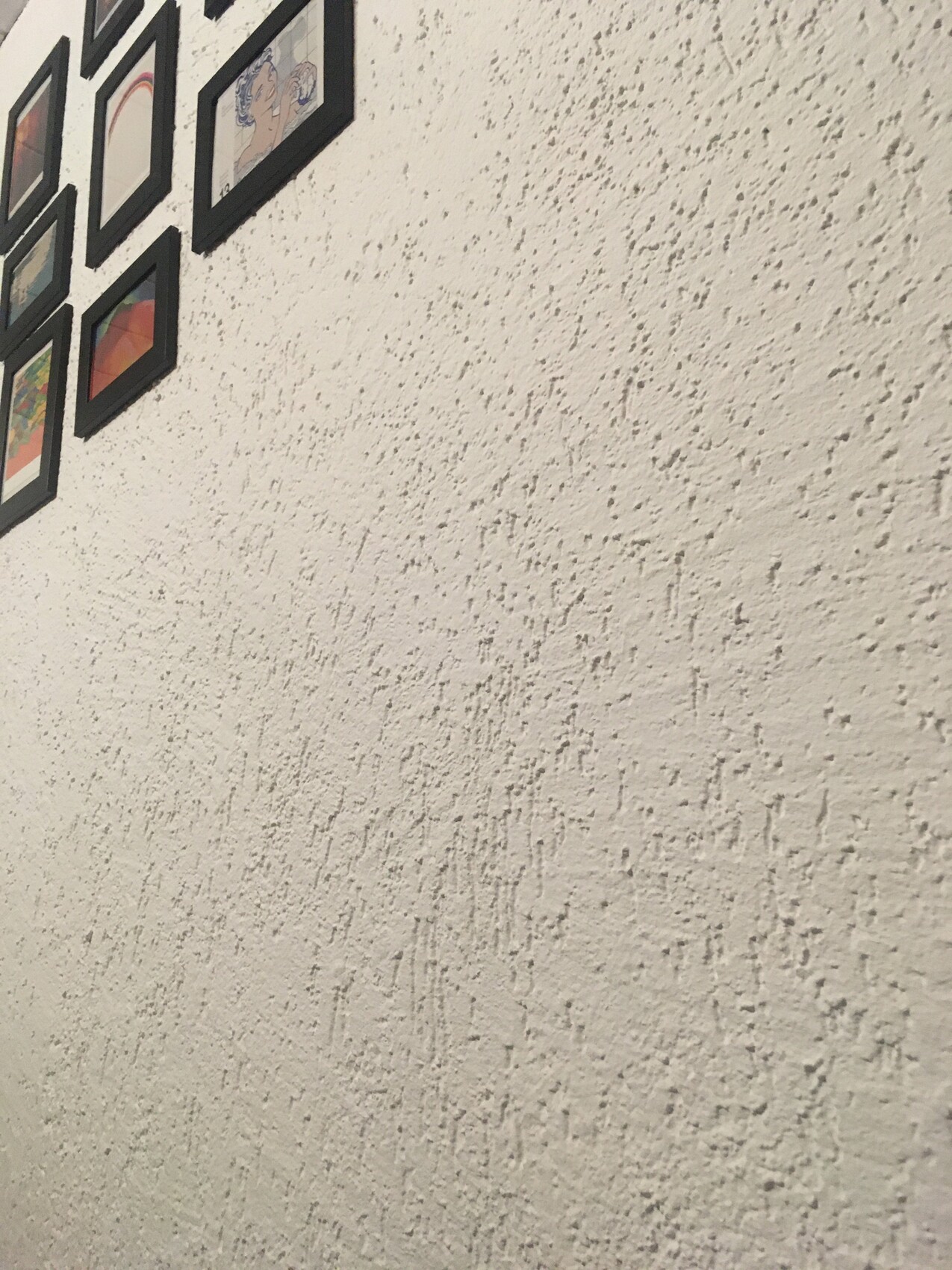 Weiße, grob strukturierte Wand mit einer Reihe schwarzer Bilderrahmen oben links.