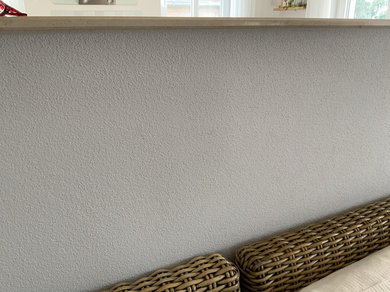 Grau texturierte Wand hinter einer Küchenbar; unten rechts zwei geflochtene Rattan-Sessel.