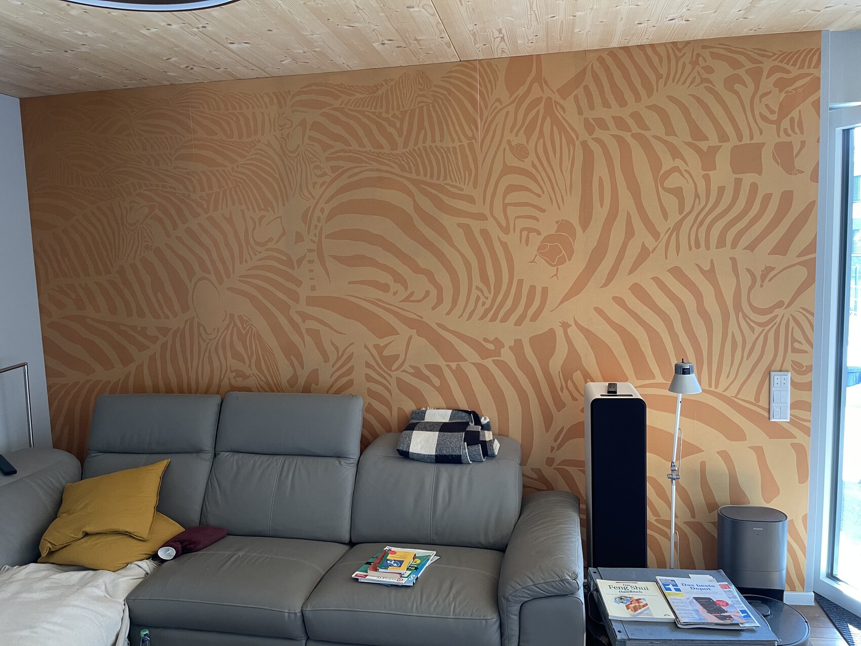 Graue Ledercouch vor orange Zebra-Wandmuster; gelbes Kissen, Decke und Zeitschriften.