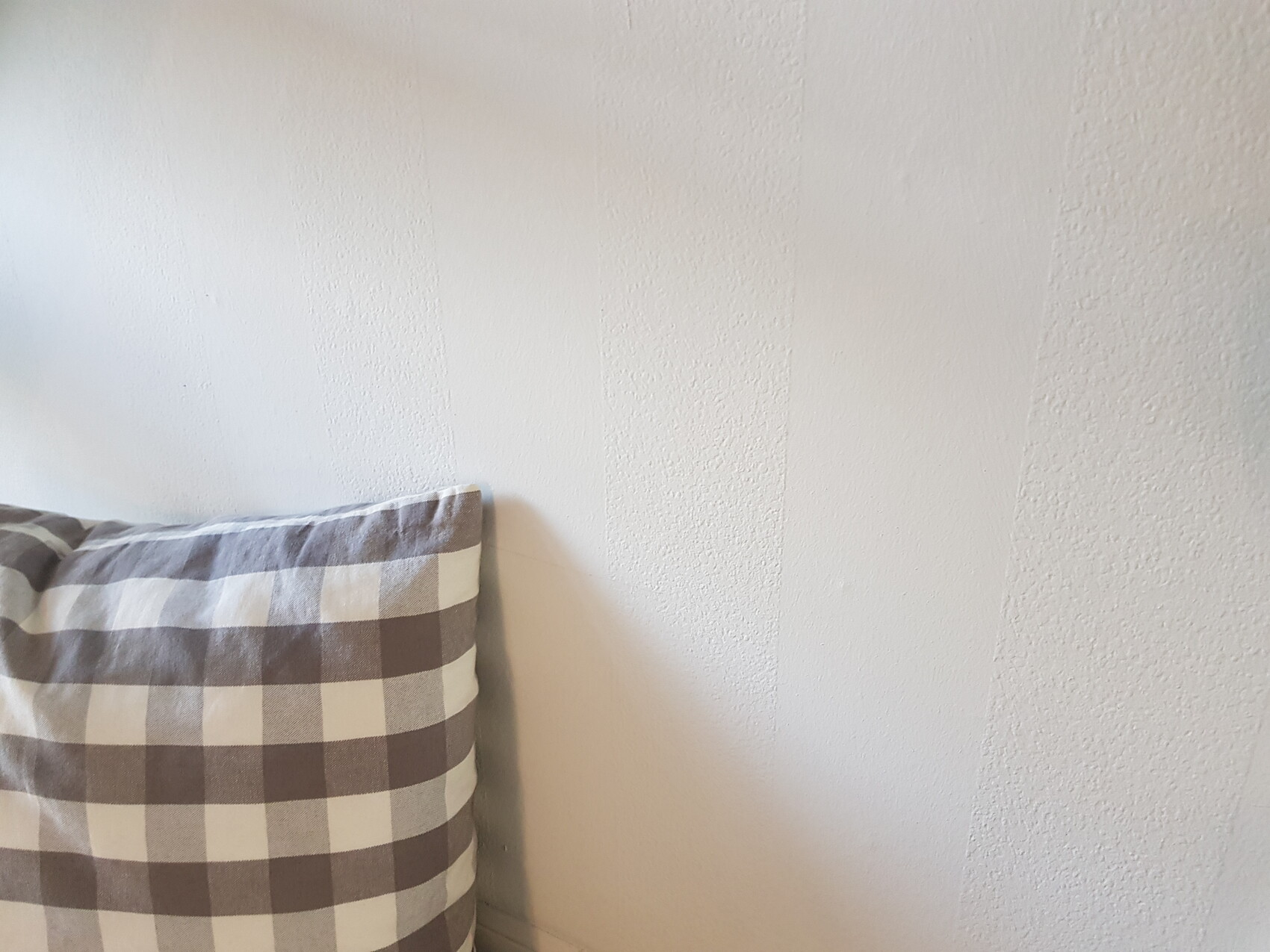 Weiße Wand mit strukturierter Oberfläche und links ein kariertes Kissen im Vordergrund.