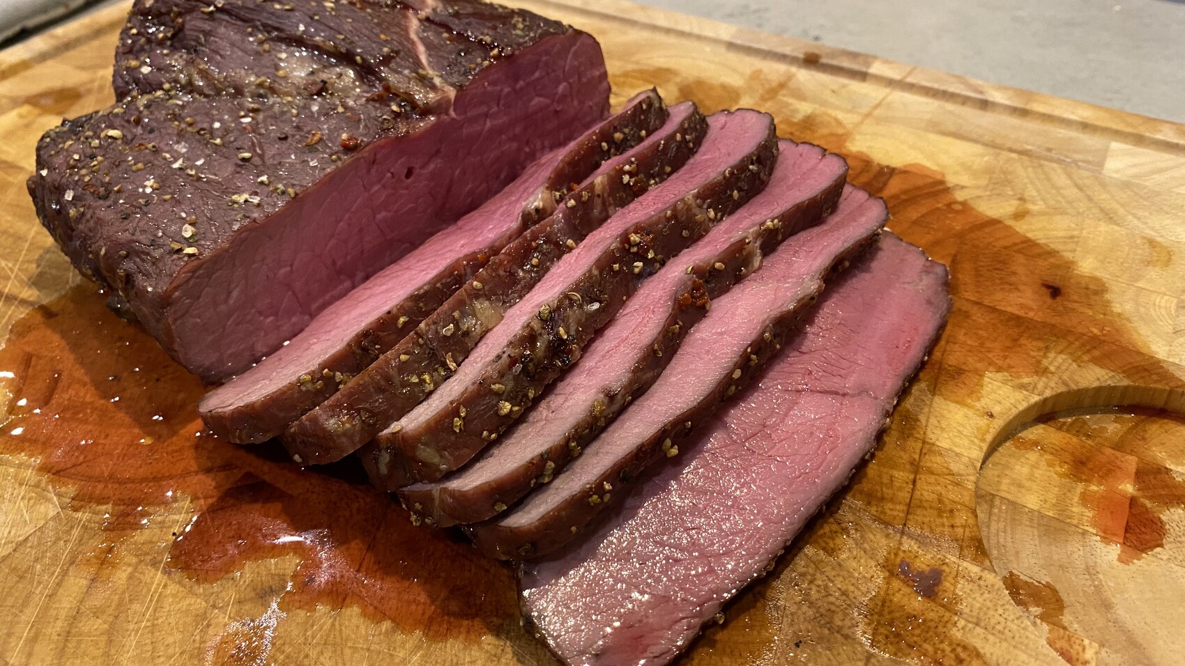 Rinderbraten in Scheiben mit Pfefferkruste, rosa innen, auf Holzbrett mit Saft.