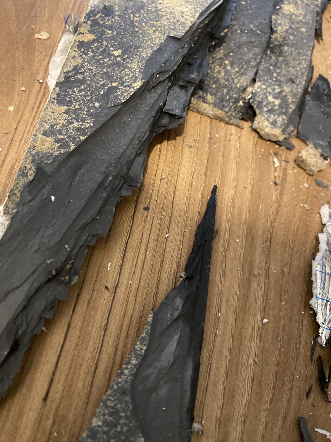 Zerbrochene schwarze Schieferstücke liegen auf Holztisch, spitzkantig und staubig.