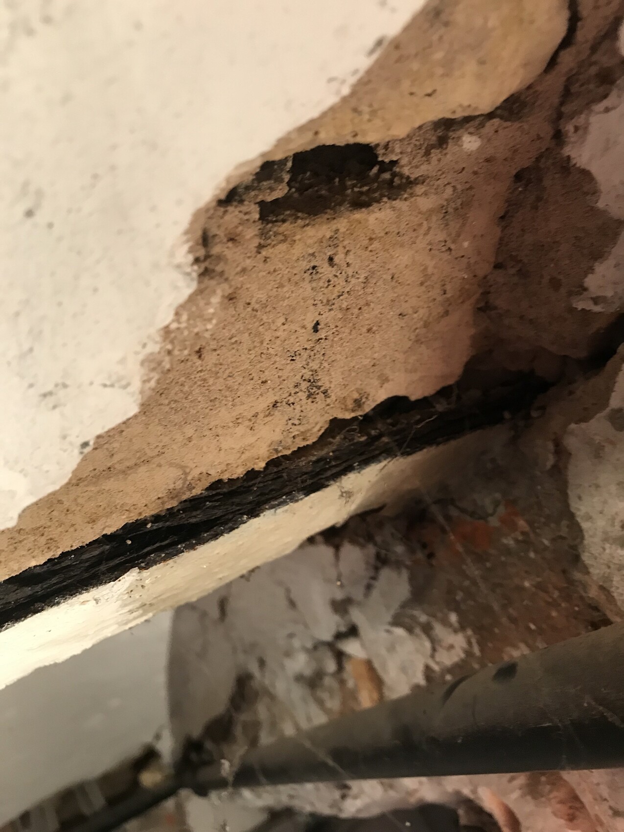 Nahaufnahme einer bröckelnden Wand mit Putzbruch, sandigen Schichten und Rohrleitung.