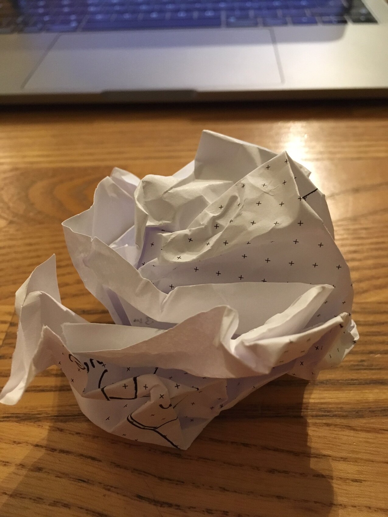 Zerknitterte Papierrose auf Holztisch vor Laptop