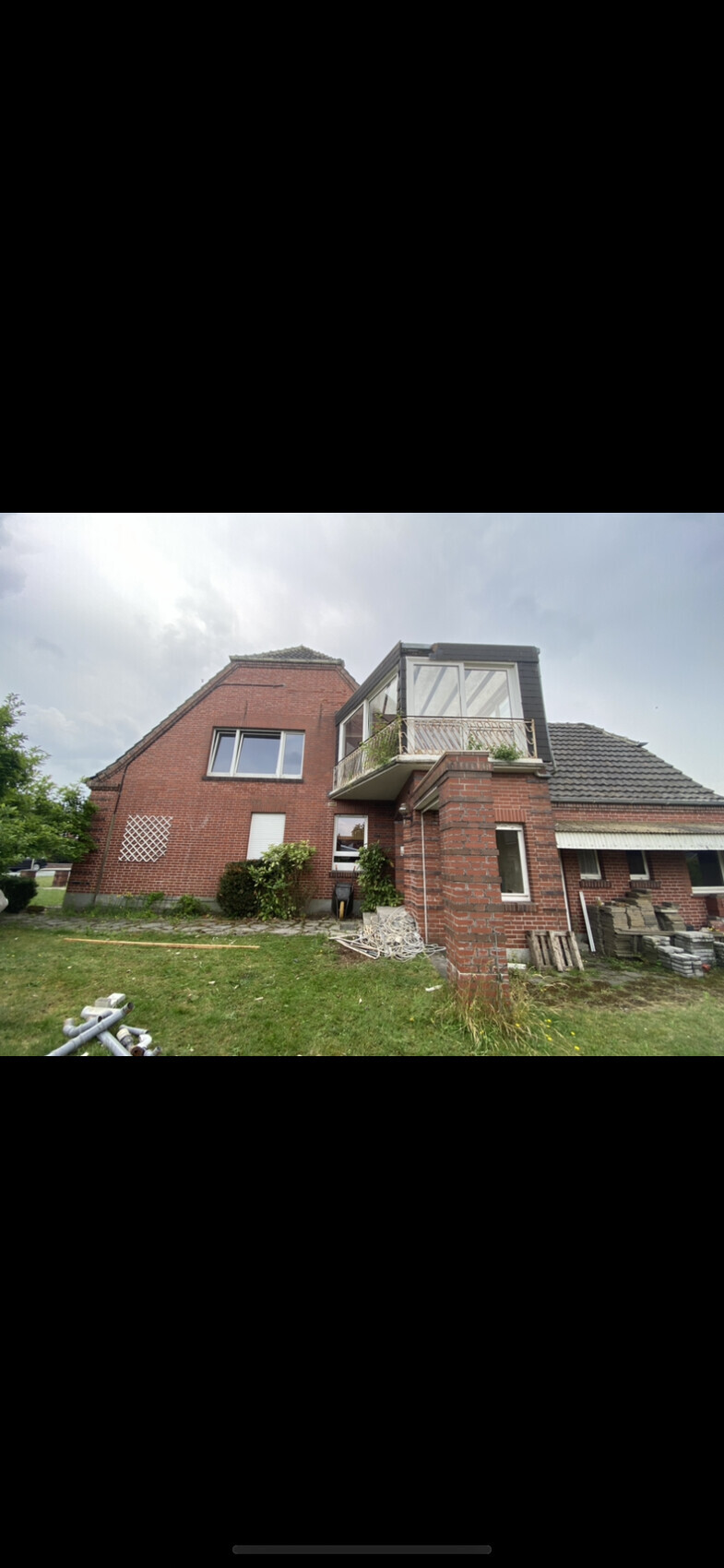 Zweistöckiges rotes Backsteinhaus mit verglaster Balkon-Veranda; Bauabfälle im Garten.