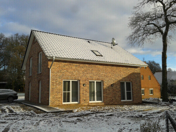 Ein rotes Ziegelhaus mit schneebedecktem Satteldach, mehreren Fenstern, Baum und Auto.
