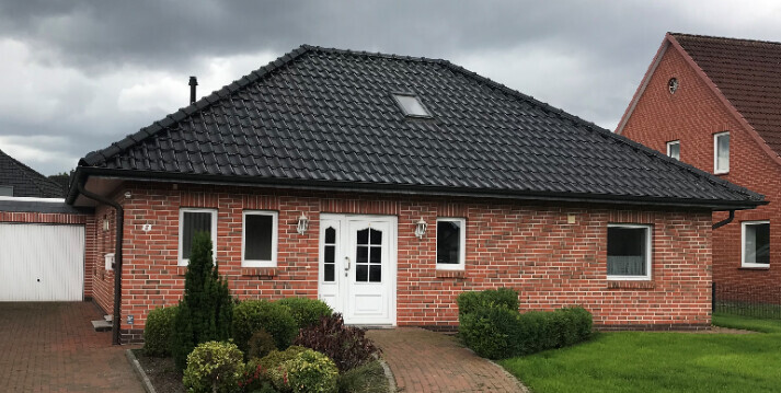 Einfamilienhaus aus rotem Backstein mit weißer Tür, Garage links, gepflegter Vorgarten