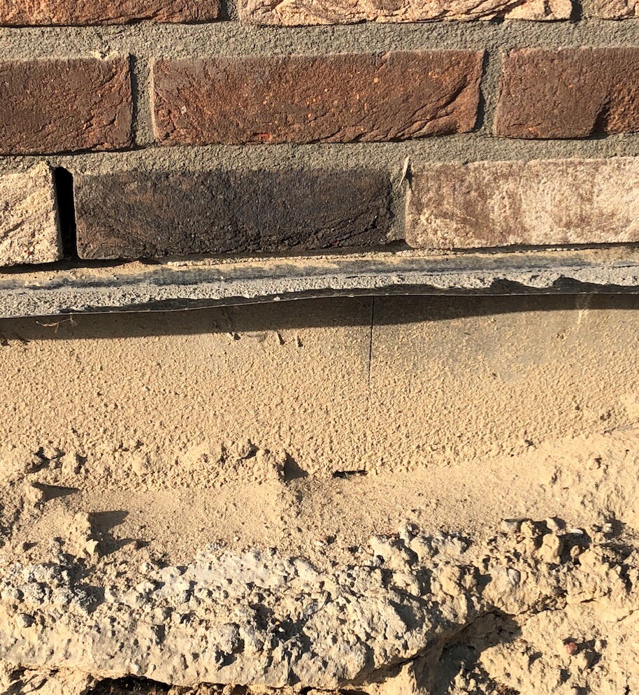 Nahaufnahme einer Ziegelwand über einem rohen Fundament und grobem Kiesboden