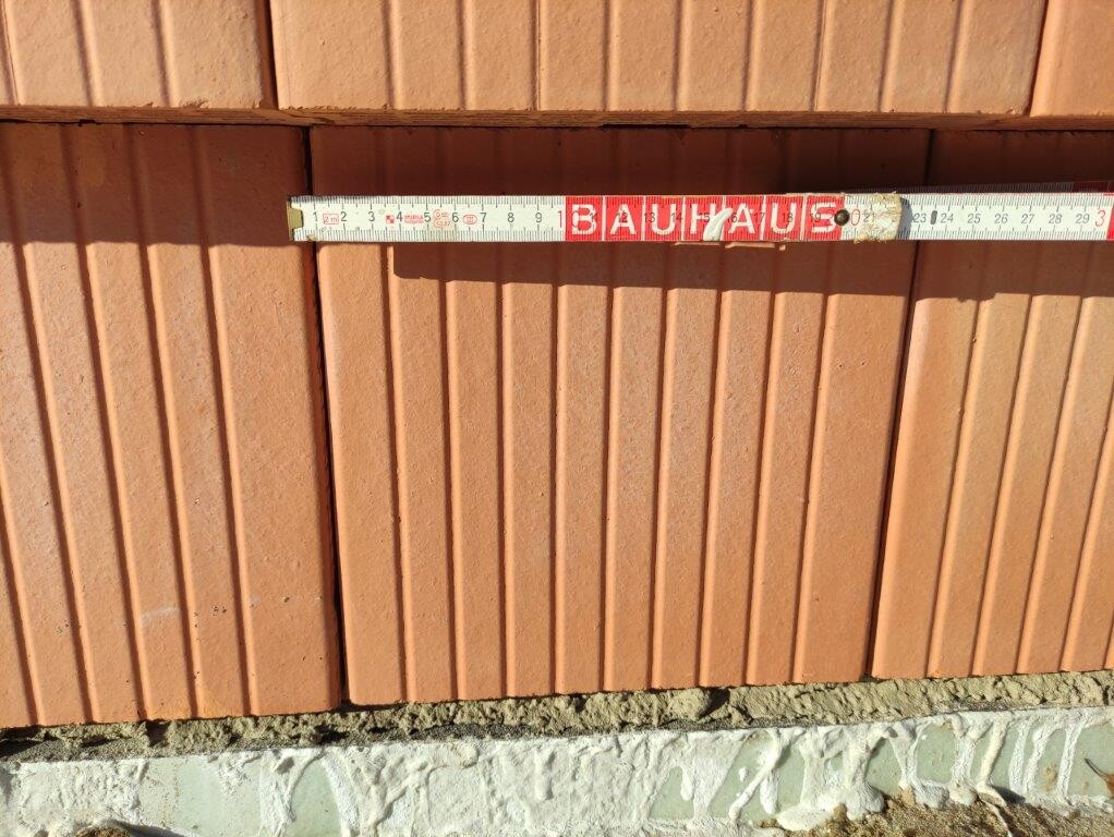 Maßband mit BAUHAUS-Aufdruck liegt horizontal an roter Ziegelwand.