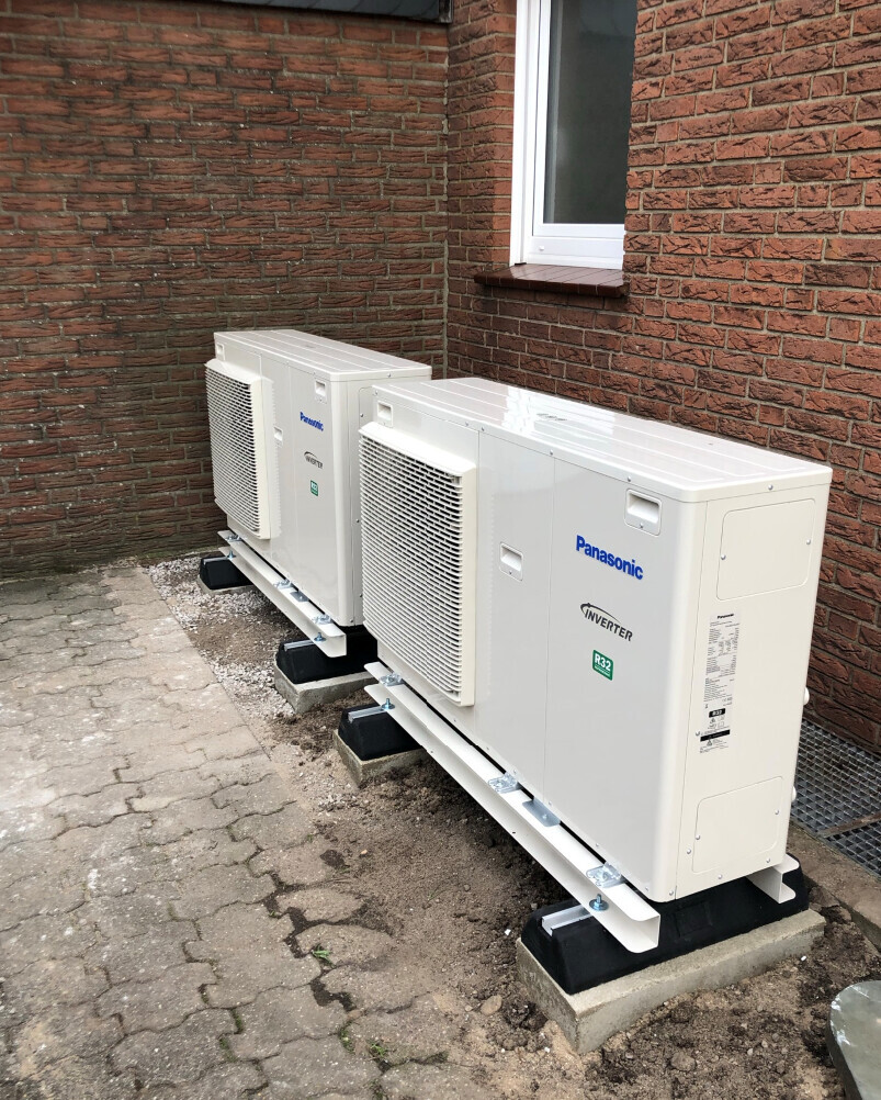 Zwei Panasonic Außen-Klimageräte auf Fundamenten neben einer roten Backsteinwand.
