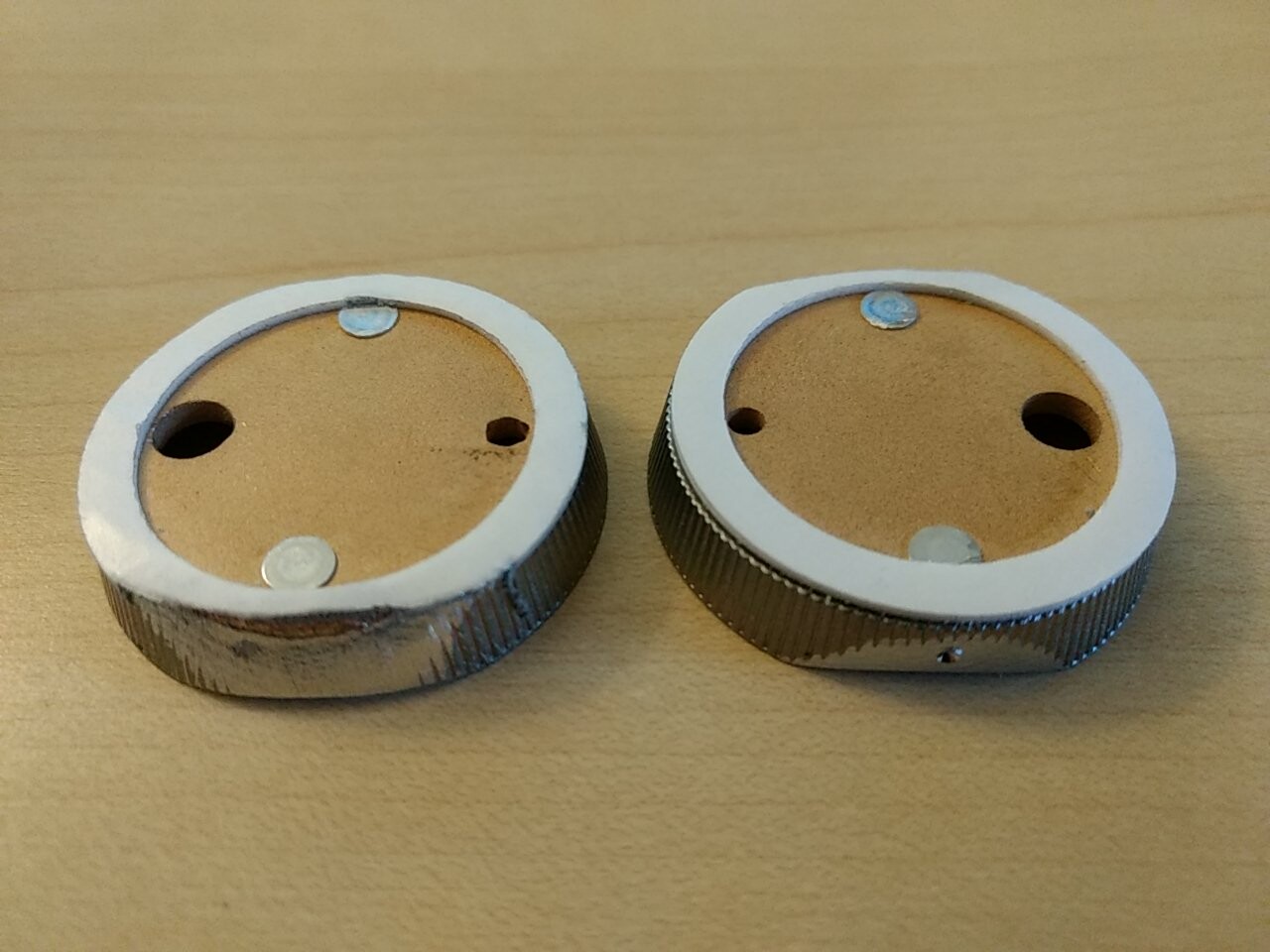 Zwei runde Drehknöpfe mit weißem Rand auf Holztisch.