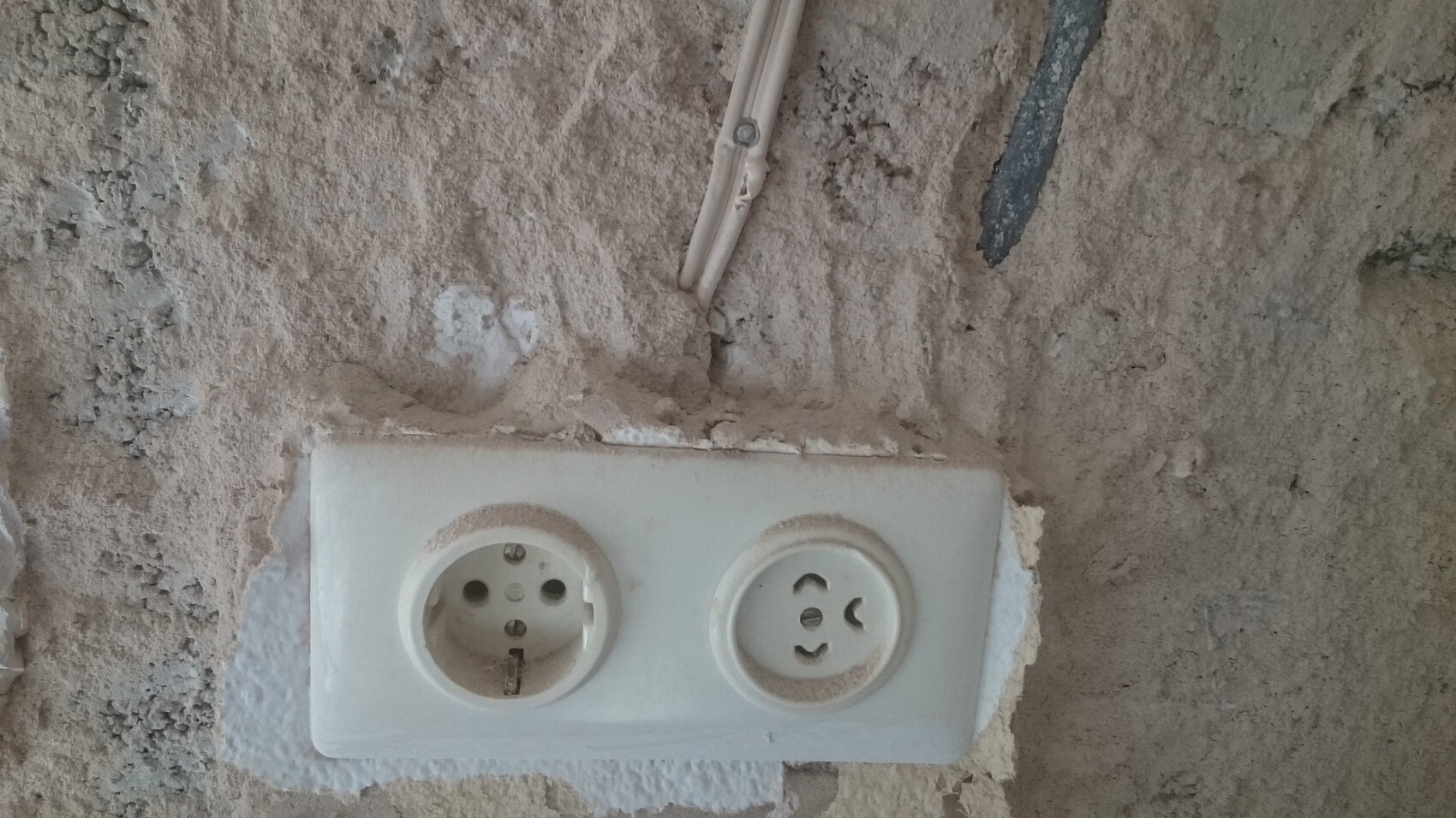 Weiße Doppelsteckdosenplatte an roher Putzwand auf Baustelle