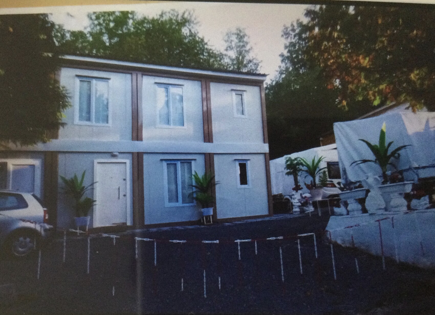 Zweistöckiges Haus mit blauer Fassade, Palmen in Töpfen und Zelt im Garten.