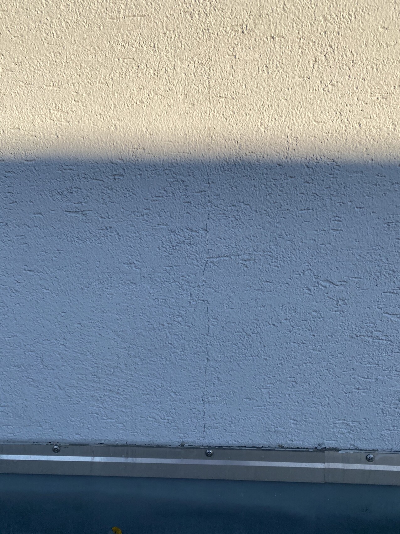 Zweifarbig verputzte Wand: oben Beige, unten Blau, Trennlinie, Riss in Mitte, Metallkante unten