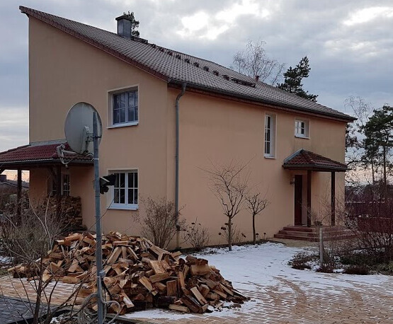 Zweigeschossiges beiges Haus im Winter mit Holzstapel und Satellitenschüssel