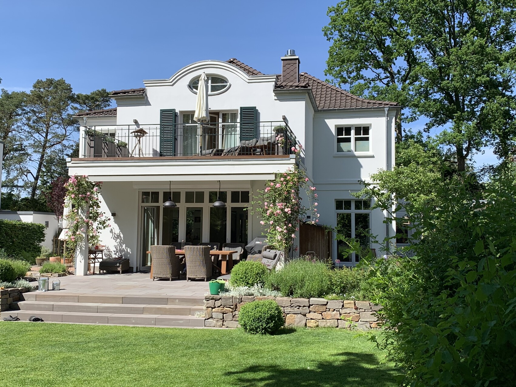 Zweistöckiges weißes Haus mit Balkon und Outdoor-Essbereich im Garten.