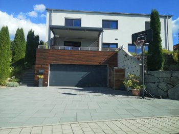 modernes-haus-mit-garage-holzverkleidung-basketballkorb-auf-gepflasterter-einfahrt.jpg